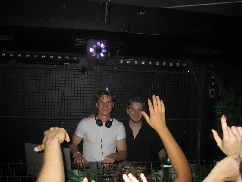 DJ Simon Beermann mit Kopfhörern am Pult, Gäste feiern mit